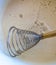 Culinary whisk for whipping with wooden handle in a white bowl with beaten eggs and sugar