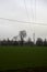 Cultivated field with trees in the distance framed by wooden pylons and over head cables on a cloudy day