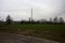 Cultivated field with trees in the distance framed by wooden pylons and over head cables on a cloudy day