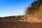 Cultivator operates on ploughed field near spring forest