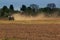 cultivator operates on ploughed field raises dust in spring