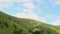 Cumulus clouds moving across blue sky, green hills, time-lapse