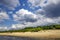 Cumulus clouds over wild sandy coast where vacationers sunbathe