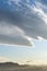 Cumulus clouds of an unusual mysterious form in the blue sky before sunset over the tops of the mountains