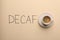 Cup of aromatic coffee and word Decaf on beige background