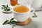 Cup of aromatic sage tea and fresh leaves on light grey table