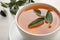 Cup of aromatic sage tea with fresh leaves on white table, closeup