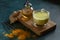 Cup of ayurvedic drink golden milk turmeric latte with curcuma powder, ginger and honey over green texture background