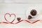 Cup of black americano coffe with gold plated chocolate in shape of heart and red satin ribbon on wooden background. Top view