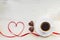 Cup of black americano coffe with gold plated chocolate in shape of heart and red satin ribbon on wooden background. Top view.