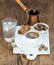 Cup of black coffee, copper pot, water with ice in glass, cinnamon sticks and cane sugar cubes on white ceramic serving