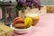 Cup of black coffee with milk and gift, lilac flowers and sweet pastel french macaroons on pink table. Top views, close-up