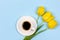 A Cup of black coffee on a saucer and a bouquet yellow tulips flowers on a blue background top view.