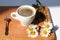 A cup of black coffee, silver spoon, branch of white daisy flowers on wooden background top view
