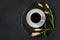 Cup of black coffee tea and fresh spring buds of lily flowers on a round slate on a black background. Romantic stylish breakfast.