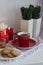 A cup of black tea with homemade cookies on a striped tablecloth, a bowl honey, a pair of decorative plants in a pot, wax candles