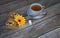 A cup of black tea and a spoon stand on a saucer on a wooden table, next to a napkin with two fresh muffins