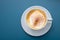 Cup of cappuccino with cocoa powder on a blue background, view directly from above, copy space