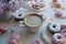 Cup of cappuccino, fresh colorful donuts, strawberry macarons and bouquet of lilac on white marble table