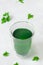 Cup with chlorophyll water on neutral grey background with green leaves