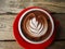 A cup of chocolate latte is served on a red saucer on a wooden table