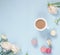 Cup of cocoa, macaroons cookies colorful in pastel colors and delicate pink ranunculus flowers on a pale blue background