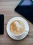 Cup of coffe with latte art standing on the wooden surface with smartphone and  tablet.