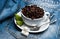 Cup with coffee beans, refined sugar and spoon on plate, denim background. Mug full of coffee beans on jeans. Fresh