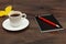 Cup of coffee, black pocketbook, pen and autumn yellow leaf on wooden table