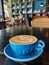 Cup of coffee in a blue cup with latte art in a beautiful aesthetic cafe on a black wooden table, morning lighting and cozy vibes