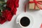 A Cup of coffee, a bouquet of red roses and a gift with a red ribbon on the table close-up.
