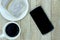 A cup of coffee, bread on white plate, smartphone on wood backgr