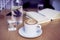 Cup of coffee cappuccino, glass of pure water, bottle on wooden table, bright interior daylight