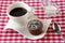 Cup of coffee, chocolate muffin with powdered sugar and milk in a gravy boat on a red white chequered tablecloth