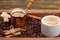 Cup of coffee, coffeepot, cinnamon sticks, anise, sugar, coffee beans on wooden background