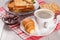 Cup of coffee and croissant on saucer, glass bowl with strawberry jam, cookies with whole grains of sunflower seeds and toasted s