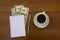 Cup of coffee, dollars, notepad and pen on wooden desk