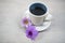 Cup of coffee with flowers. Morning coffee concept with soft purple orchid daisy flower on white table bright background.