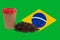 A cup of coffee and a handful of roasted coffee beans against the background of the flag of Brazil