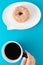 A cup of coffee held by a hand and a doughnut on plate shaped like text bubble, on blue background