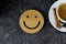 A cup of coffee is the key to a good mood. Wooden smiley on a dark, black, textural background. On the edge you can see a white