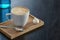 Cup of coffee on the little board over black background. Latte art. Little coffee mug and spoon.