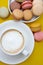 Cup of coffee and macaroons on colorfu lyellow background. top view