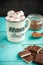 A cup of coffee with marshmallow, chocolate bar and cocoa on green wooden background. Drinks and sweets