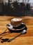 A cup of coffee with marshmallows on a wooden table background. A cocoa drink in a porcelain cup with a metal spoon.