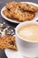 Cup of coffee with milk and fresh baked oatmeal cookies on white plate. Delicious crunchy dessert