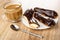 Cup of coffee with milk, whole eclairs and halves of eclair with chocolate in plate, teaspoon on wooden table