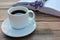 Cup of coffee, open book and bunch of purple lavender flowers on wooden table in the garden.