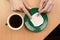 A cup of coffee and a painted cookie on a saucer. A woman`s hand draws a cookie