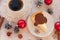 A cup of coffee, a piece of an appetizing cheese cake with melted chocolate on it, silver cones, cinnamon sticks and Christmas-t